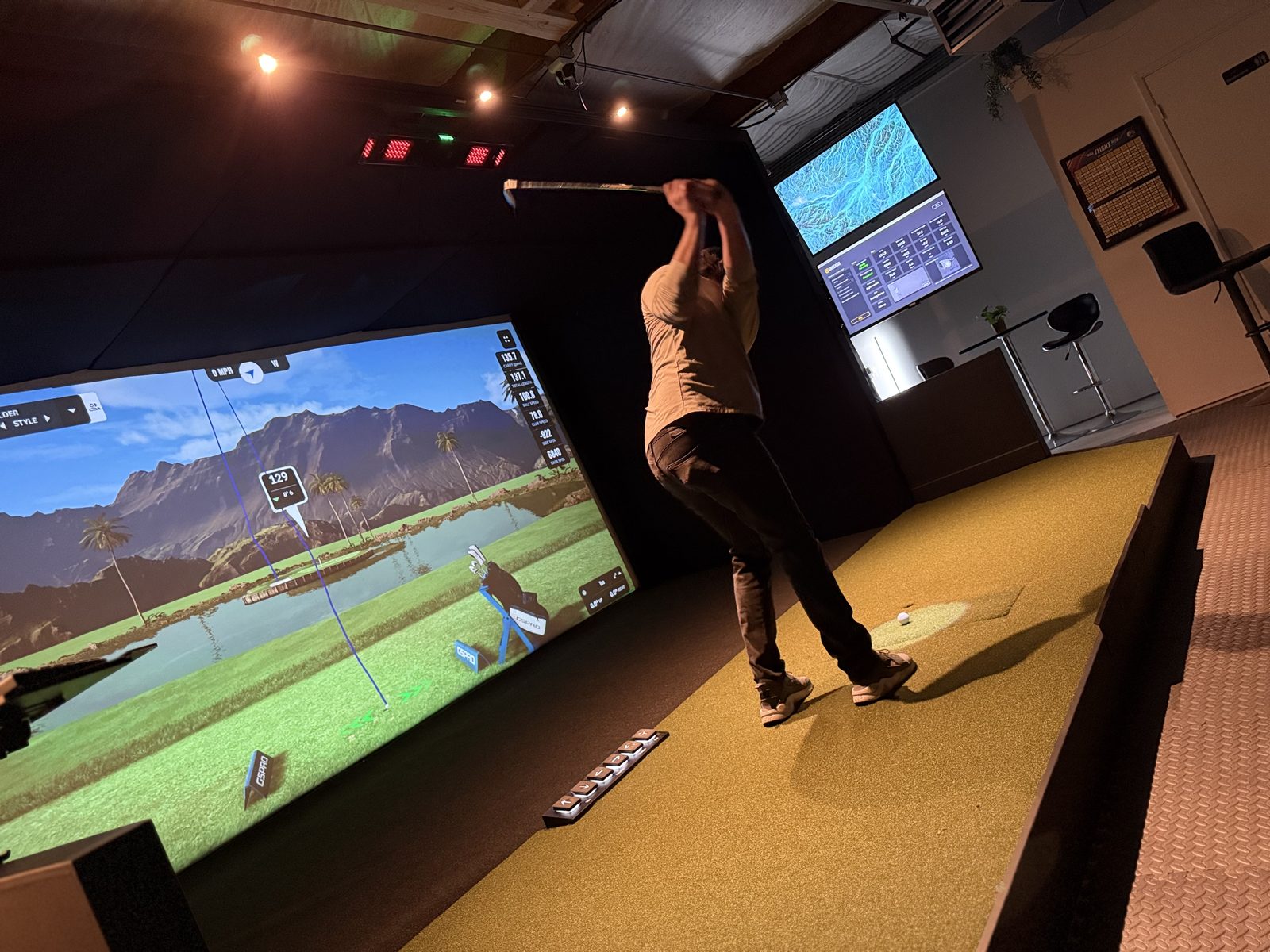 A golfer mid-swing in the Launch House Hillsboro bay, the simulator screen lit in front of them